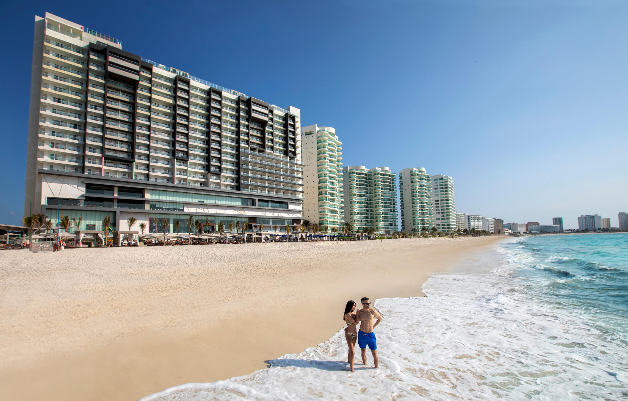 a man and woman standing on a beach with buildings in the background