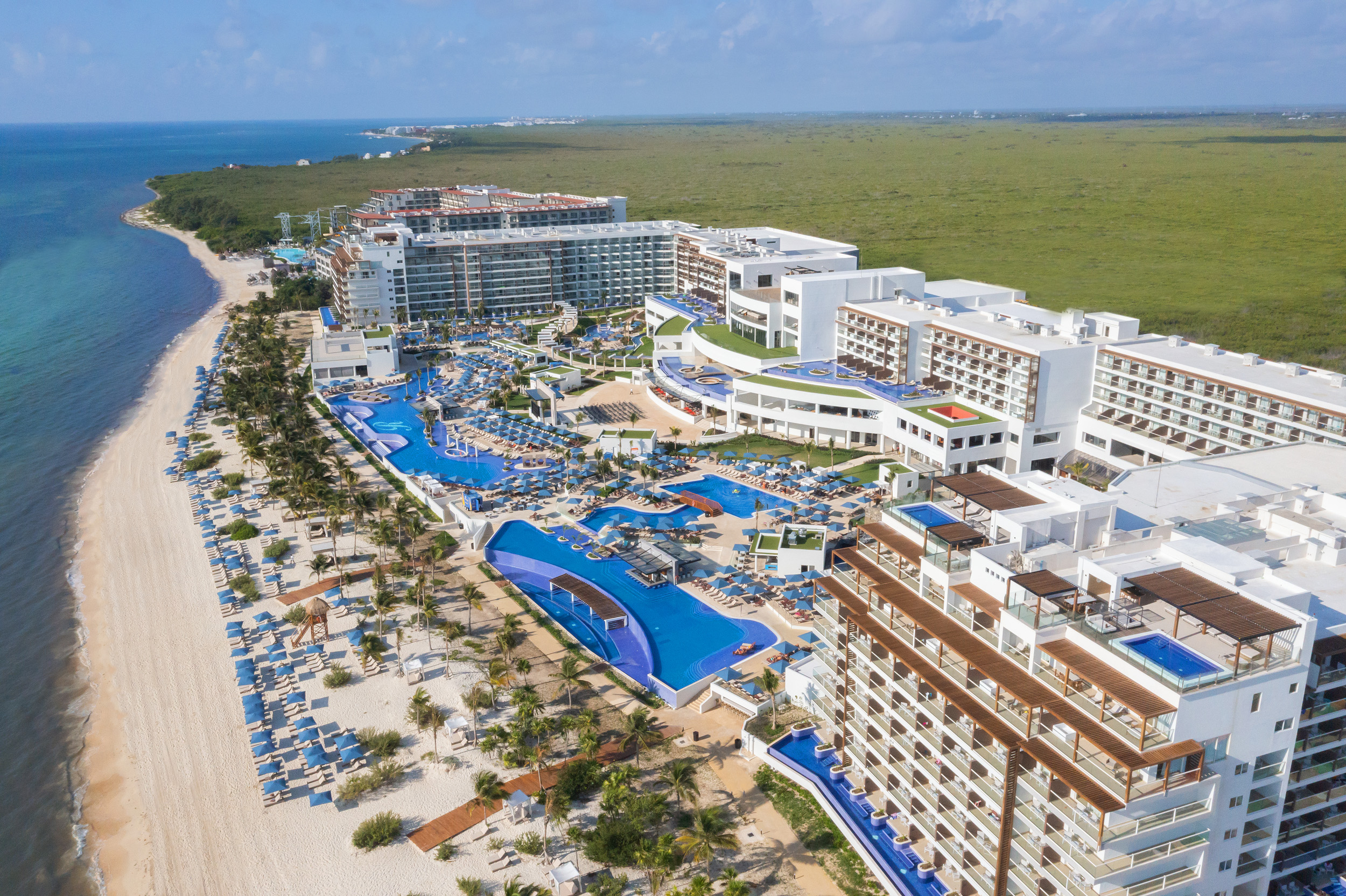 a large white building with blue pools and trees on a beach