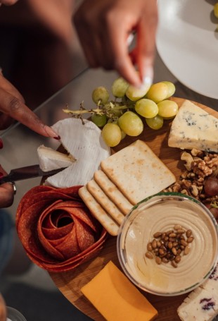 a person cutting a cheese board with grapes and cheese