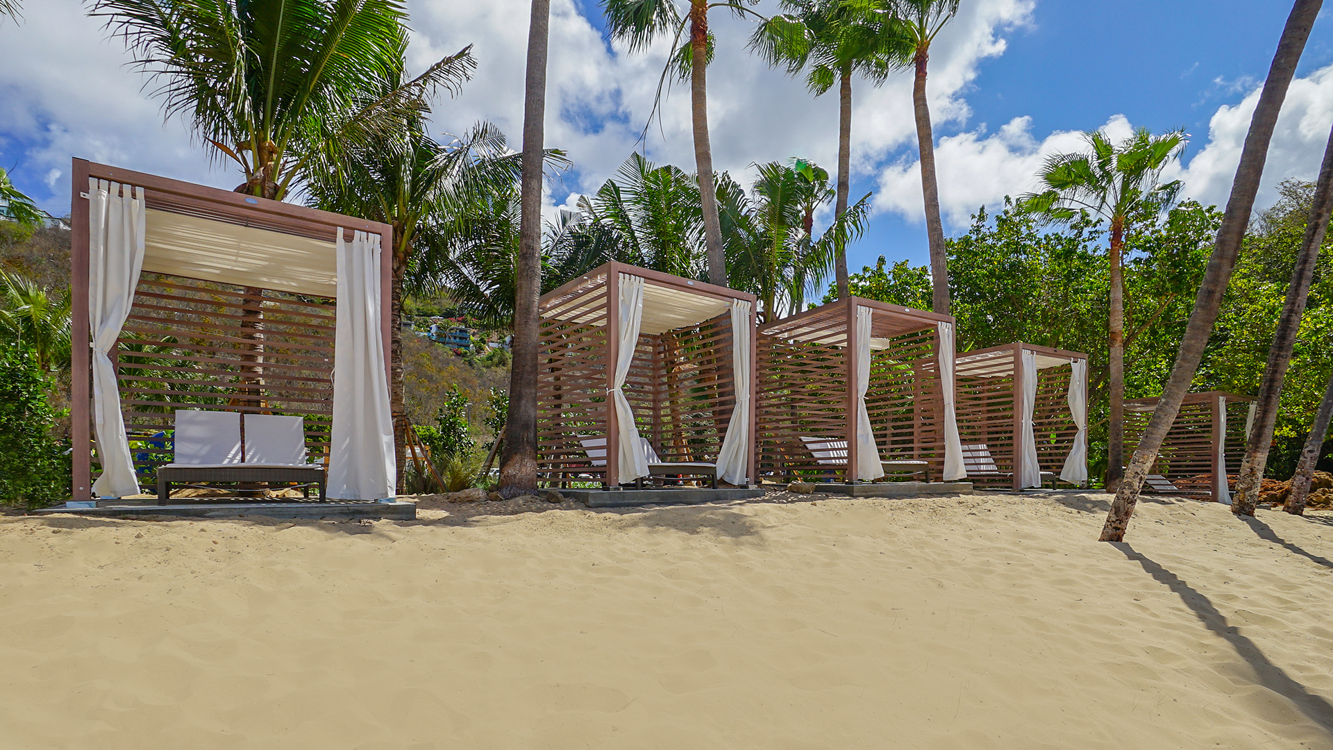 a group of wooden structures with white curtains on a sandy beach