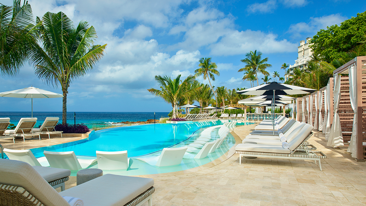 a pool with chairs and umbrellas by the ocean