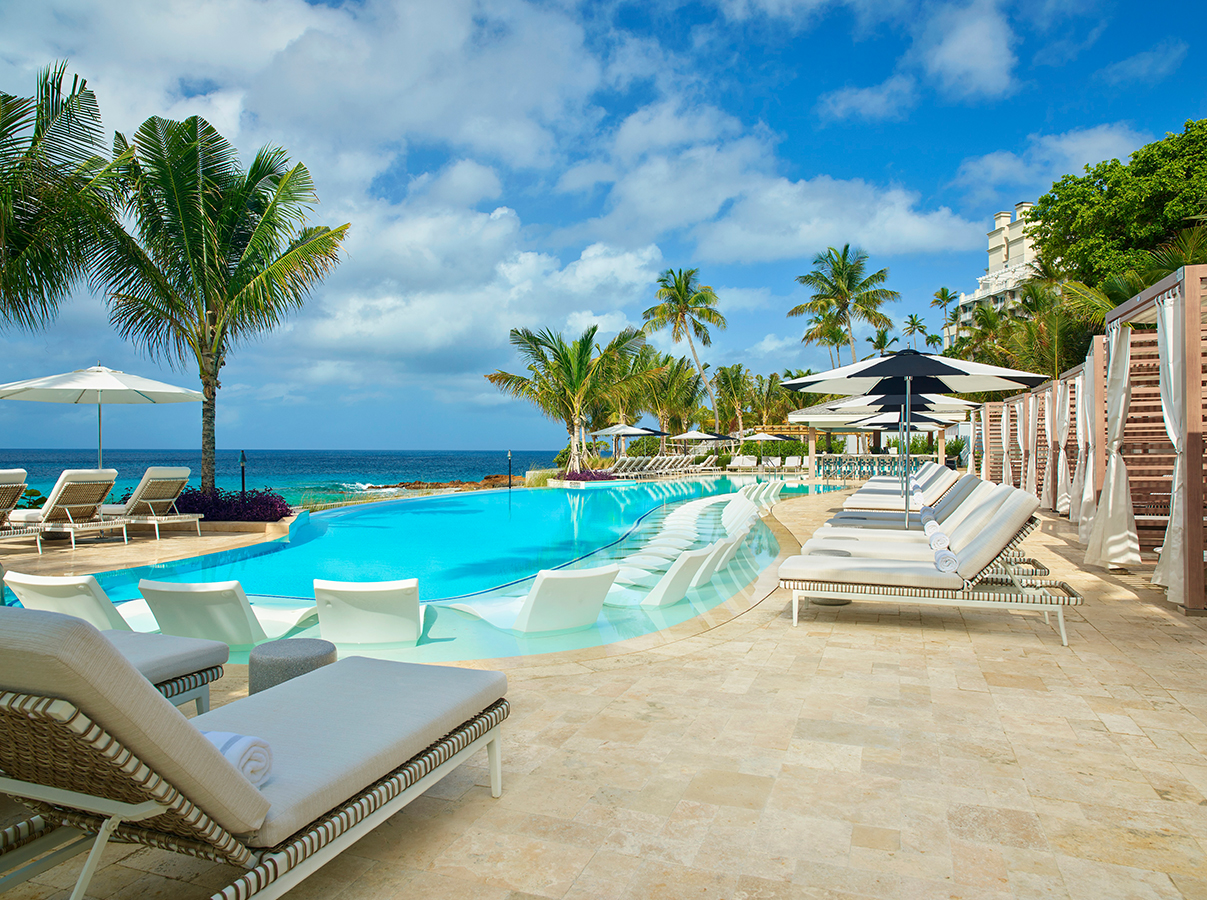a pool with lounge chairs and umbrellas by the ocean