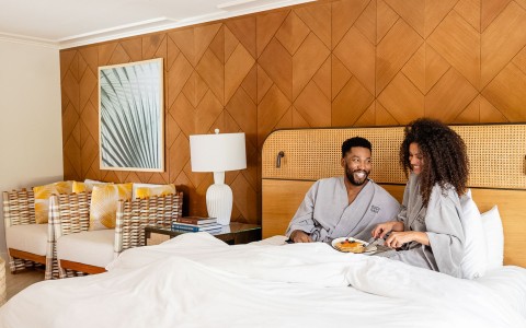 a man and woman sitting in bed with food on plate