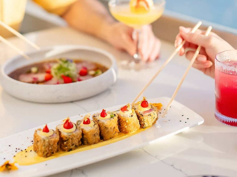 a person holding chopsticks to a plate of sushi