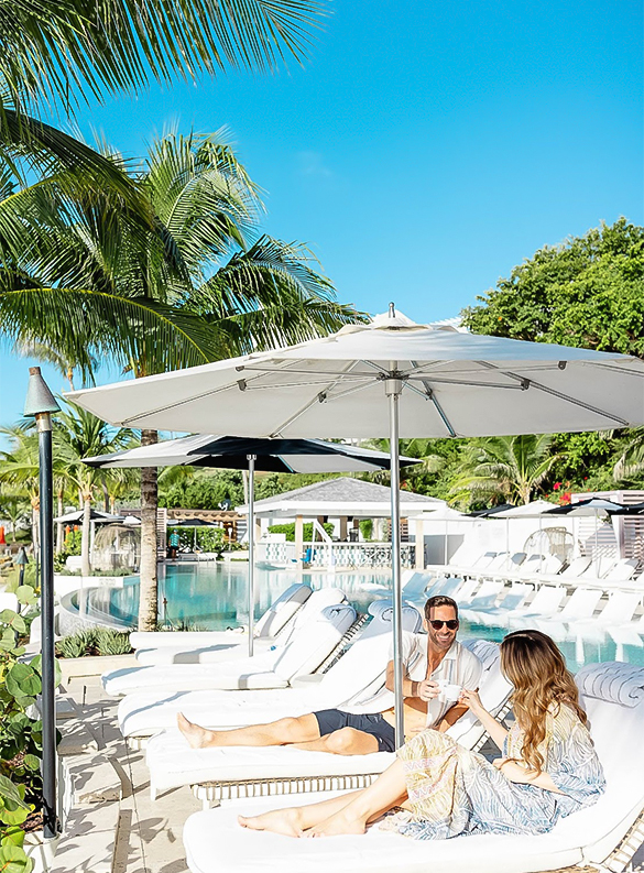 a couple sitting under a white umbrella by a pool