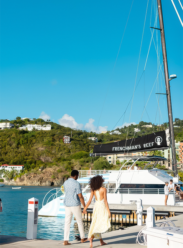a man and woman holding hands on a dock with a boat and buildings in the background