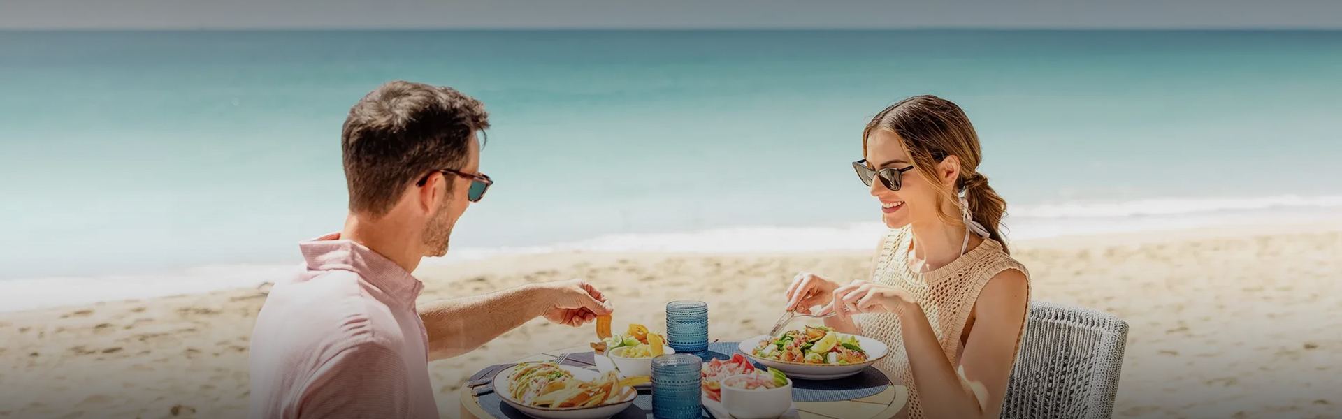 a man and woman eating at a table on a beach