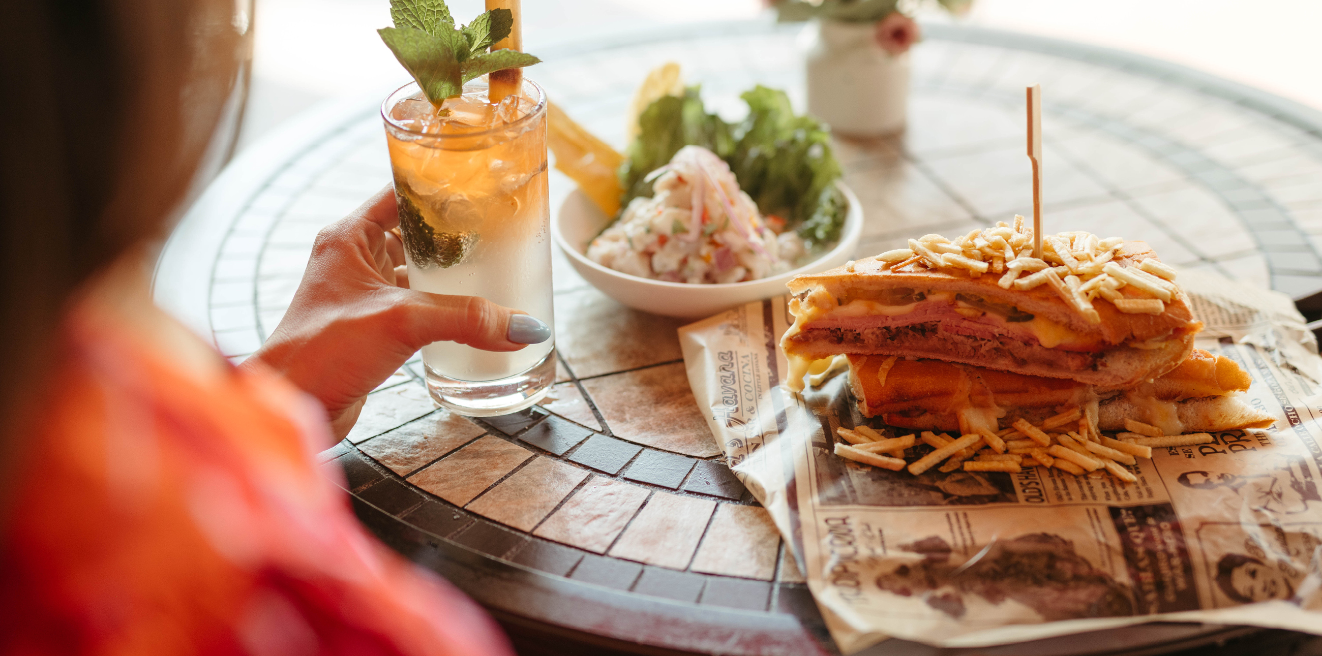 a hand holding a glass of beer next to a tray of food