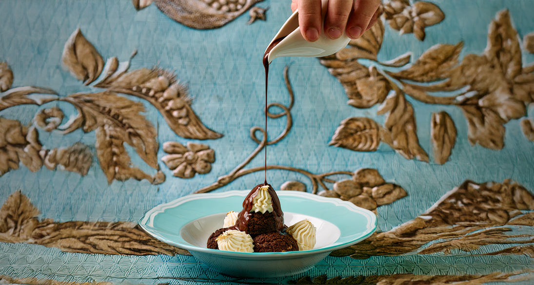 a person pouring chocolate syrup on a plate of dessert