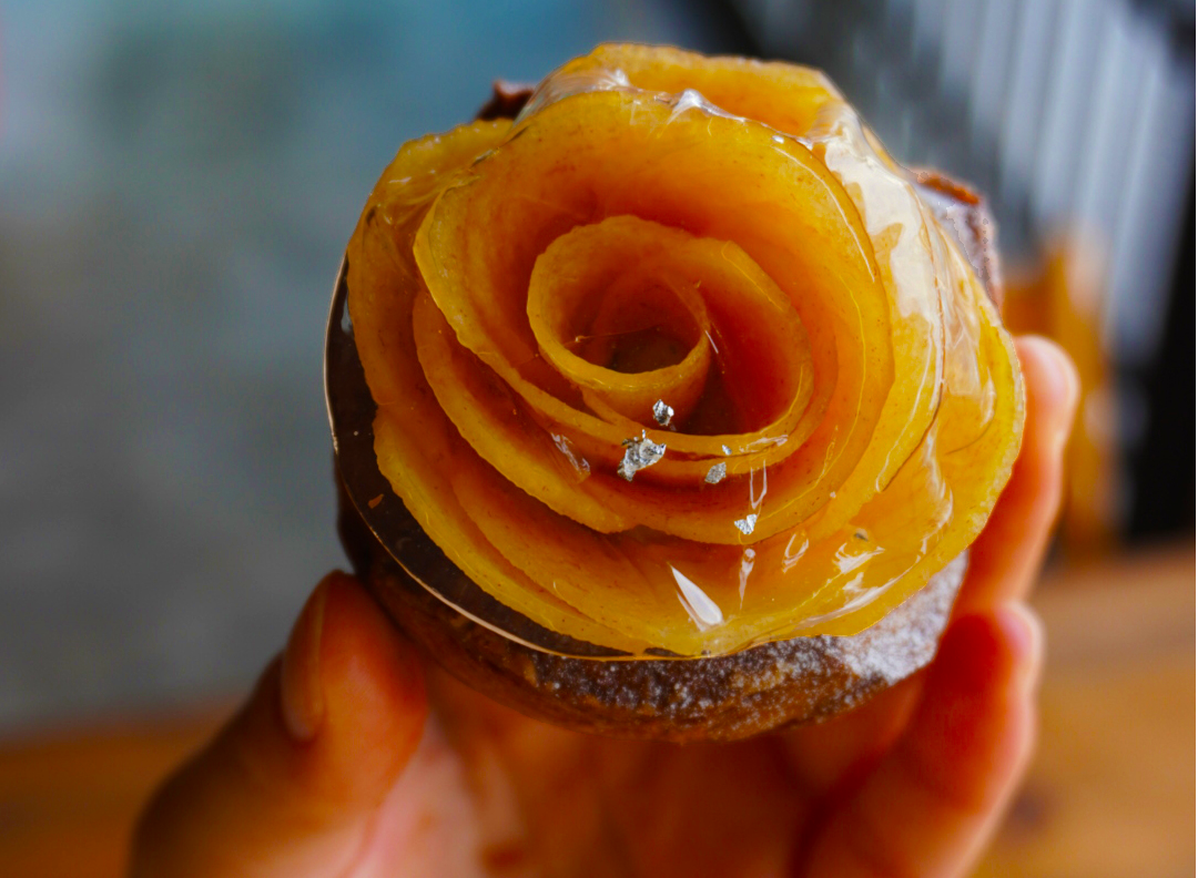 a hand holding a pastry with a rose made of fruit