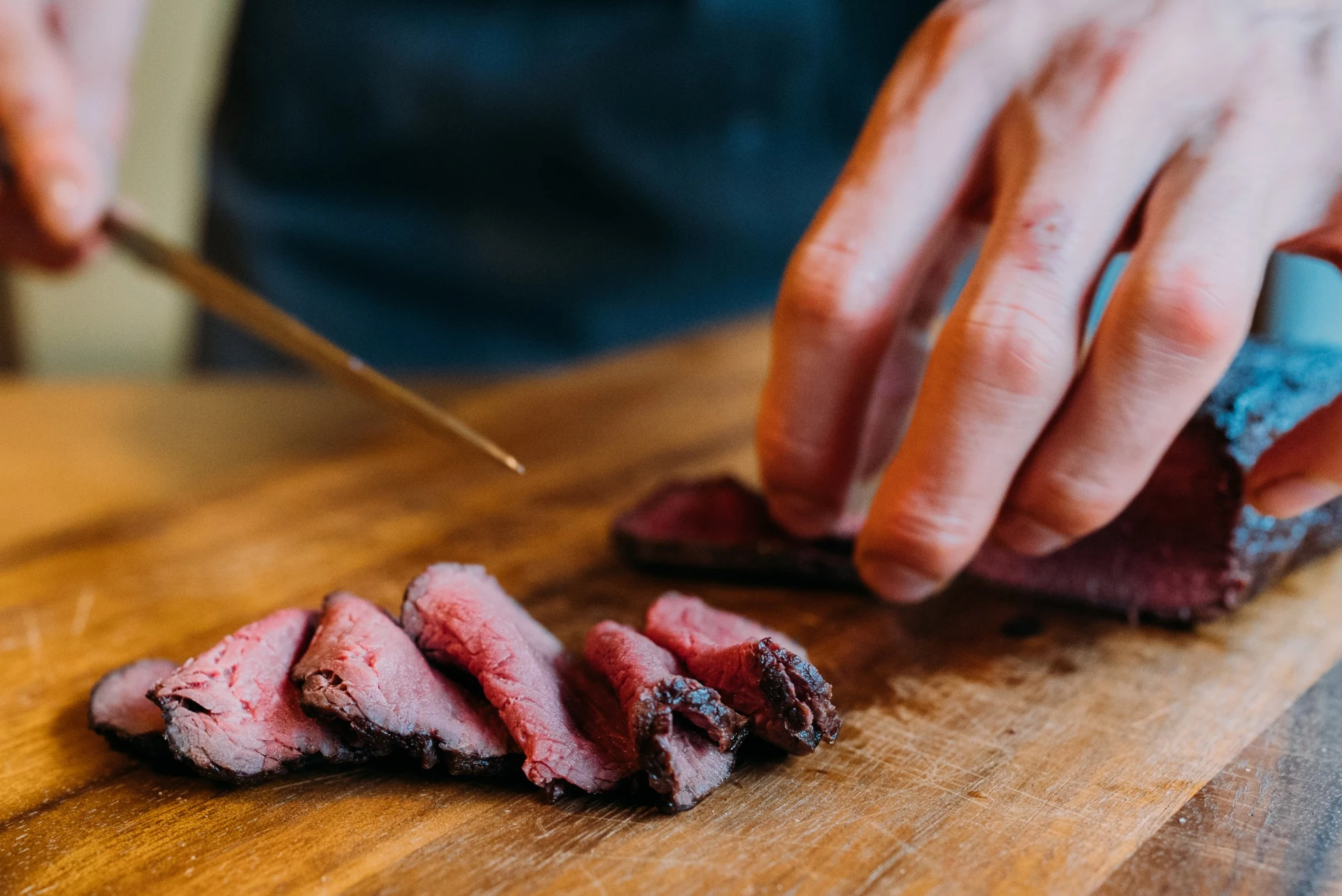 a person cutting meat on a wooden surface