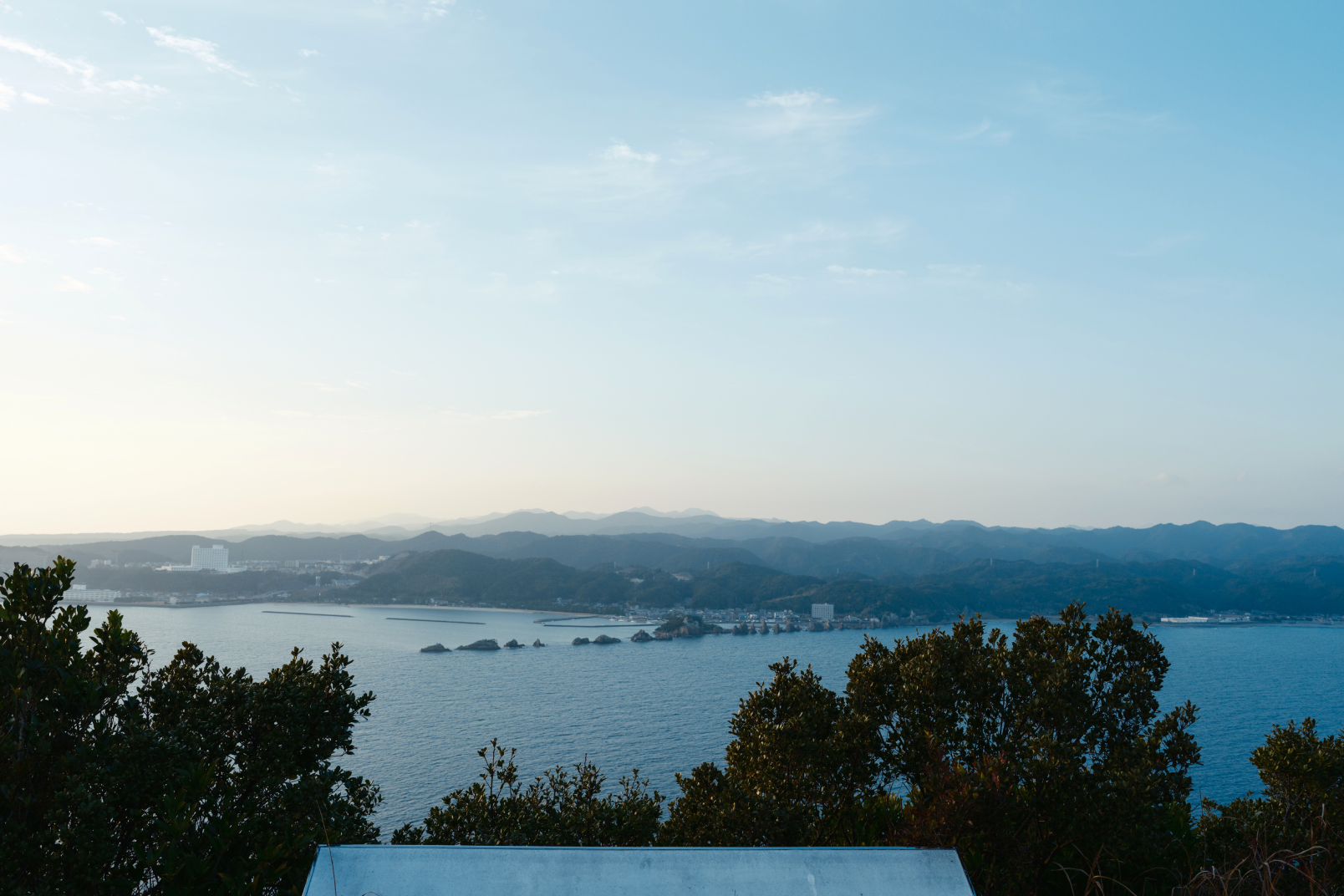 a view of a body of water and trees with buildings and mountains in the background