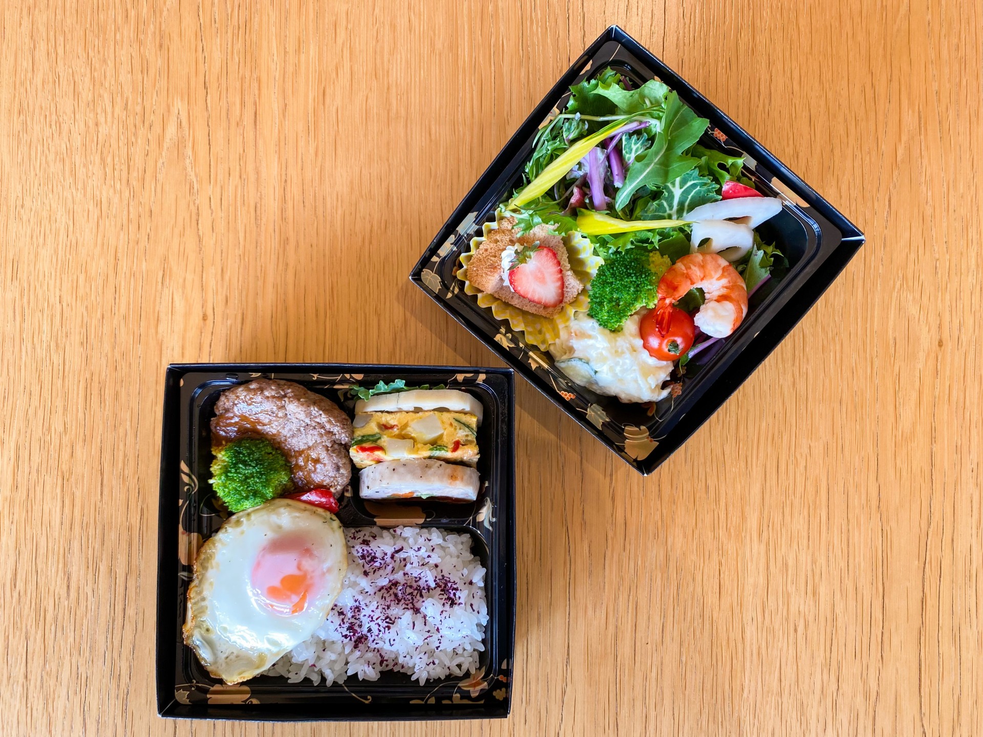a two square black containers with food on a wood surface