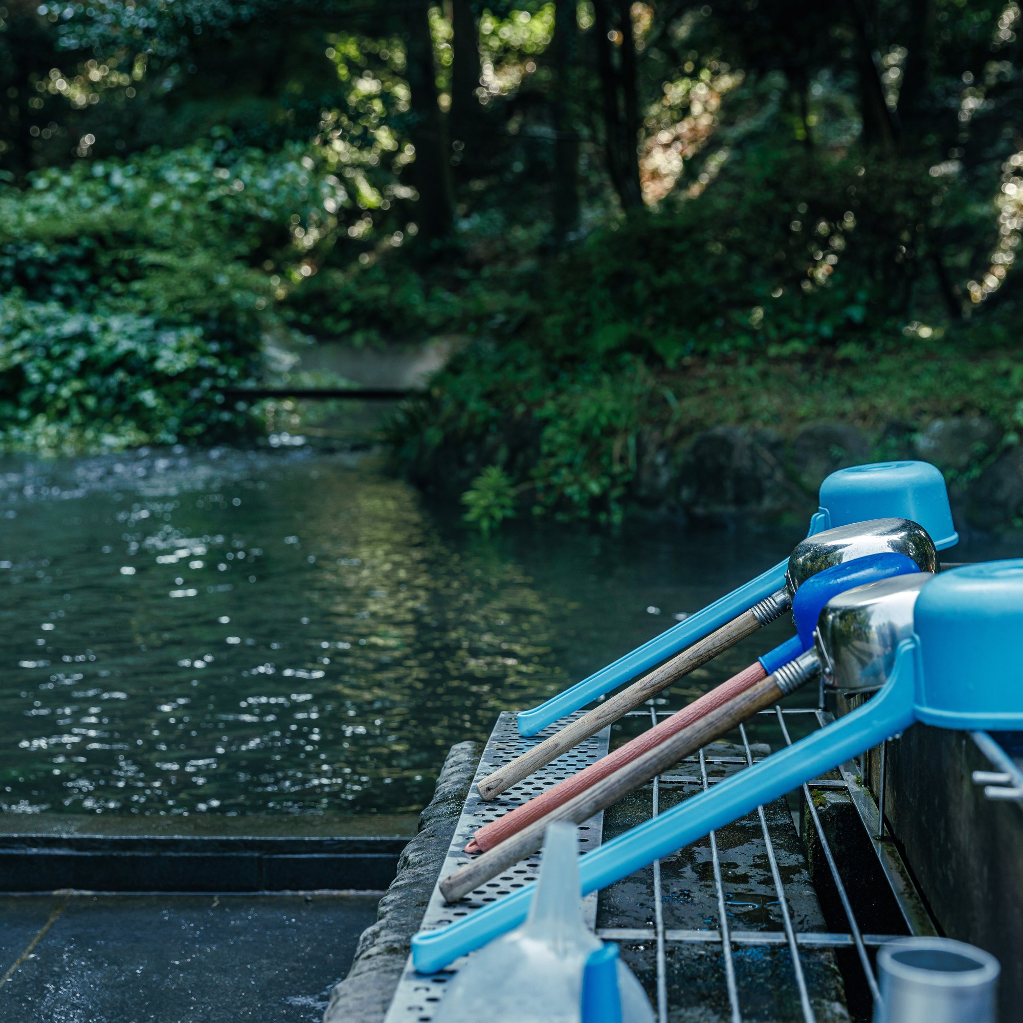 a group of blue measuring cups and a bucket on a shelf next to a body of water