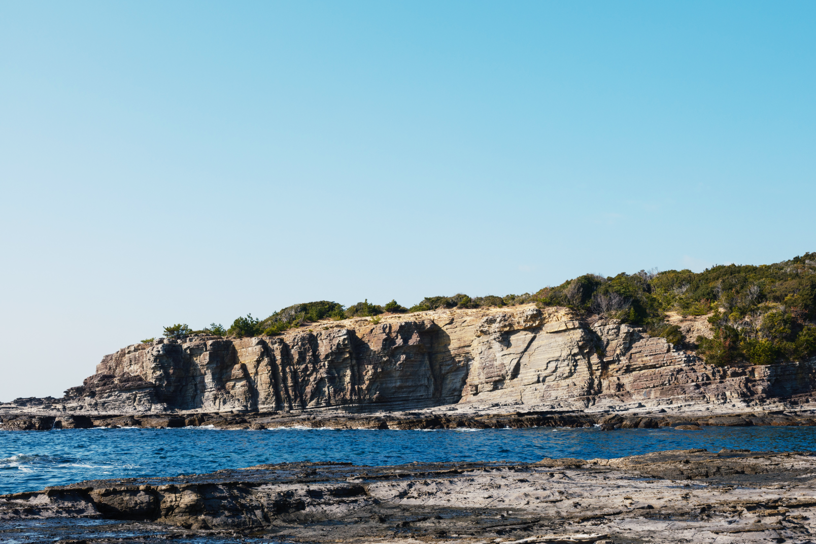 a rocky cliff with blue water and blue sky