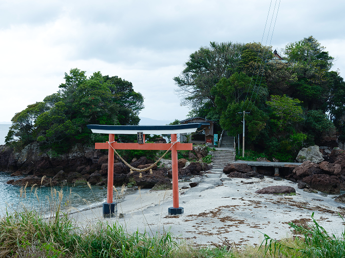 a red and white gate on a beach with trees and a building