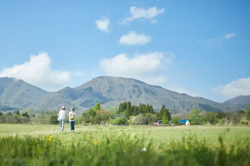 two people walking in a field with mountains in the background
