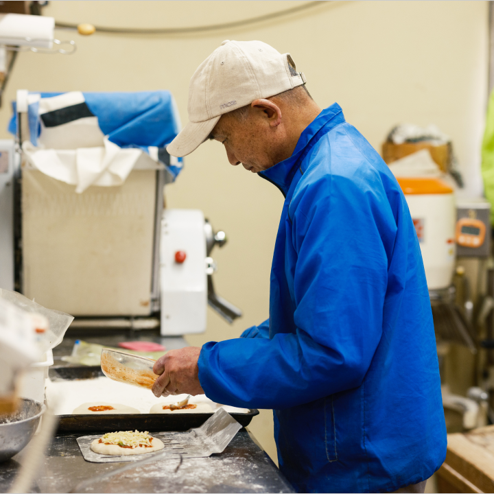 a man in a blue jacket making pizza