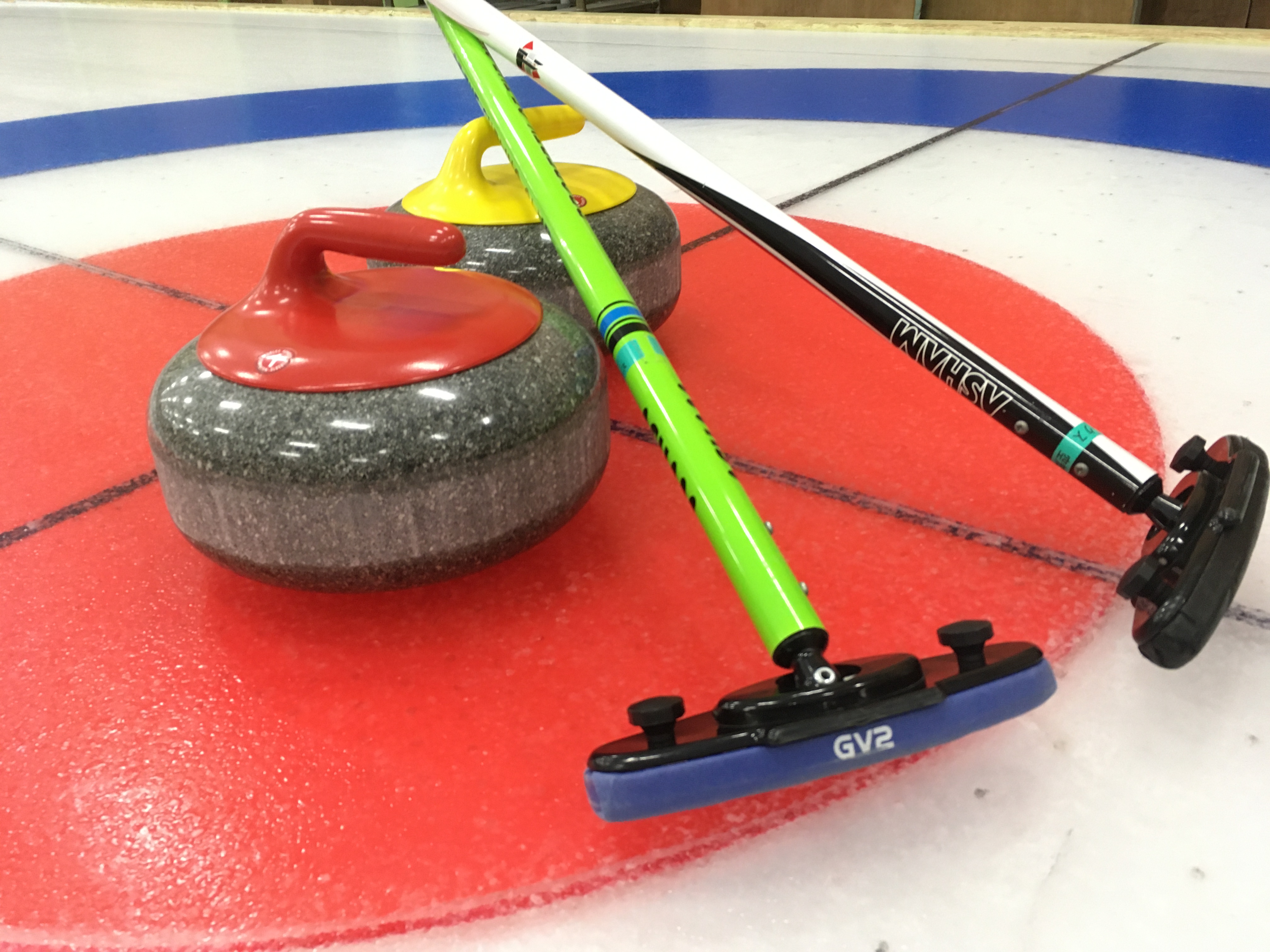 curling stones and curling sticks on a red and blue surface