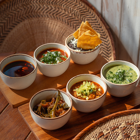 a group of bowls of soup and chips on a wooden surface