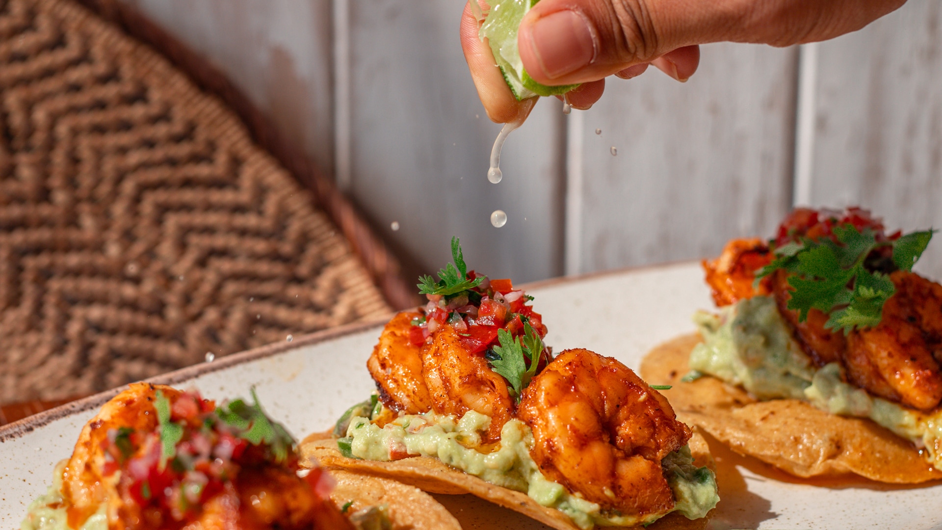 a hand squeezing a lime over a shrimp taco