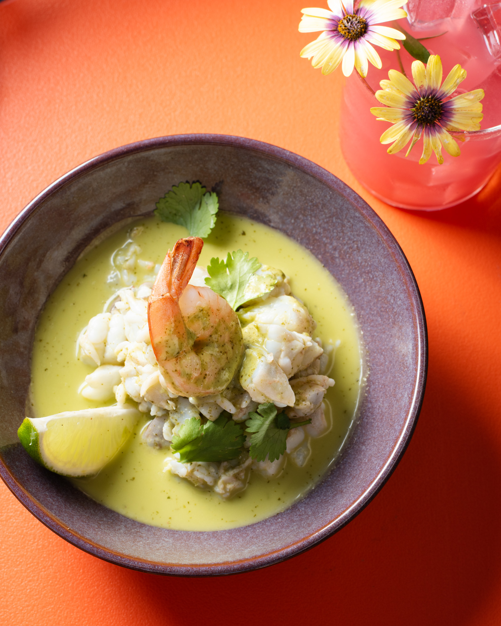 a bowl of soup with shrimp and lime wedges