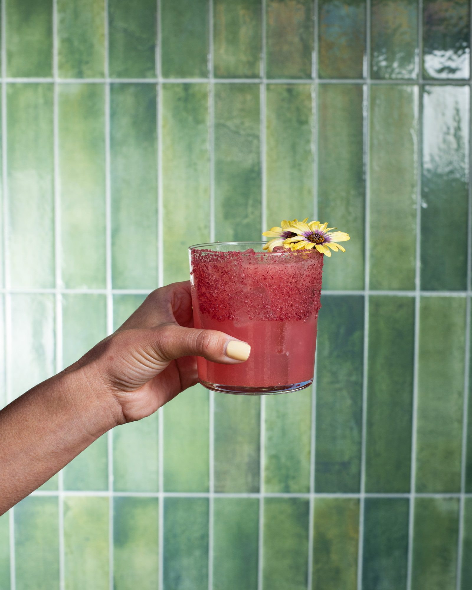 a hand holding a glass with a drink and a flower on it