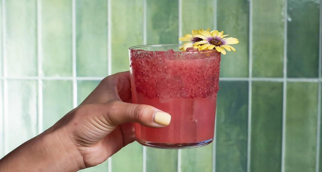 a hand holding a drink with a flower on top