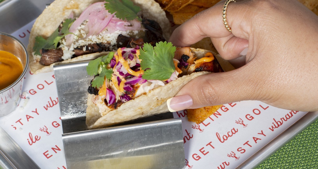 a hand holding tacos on a tray