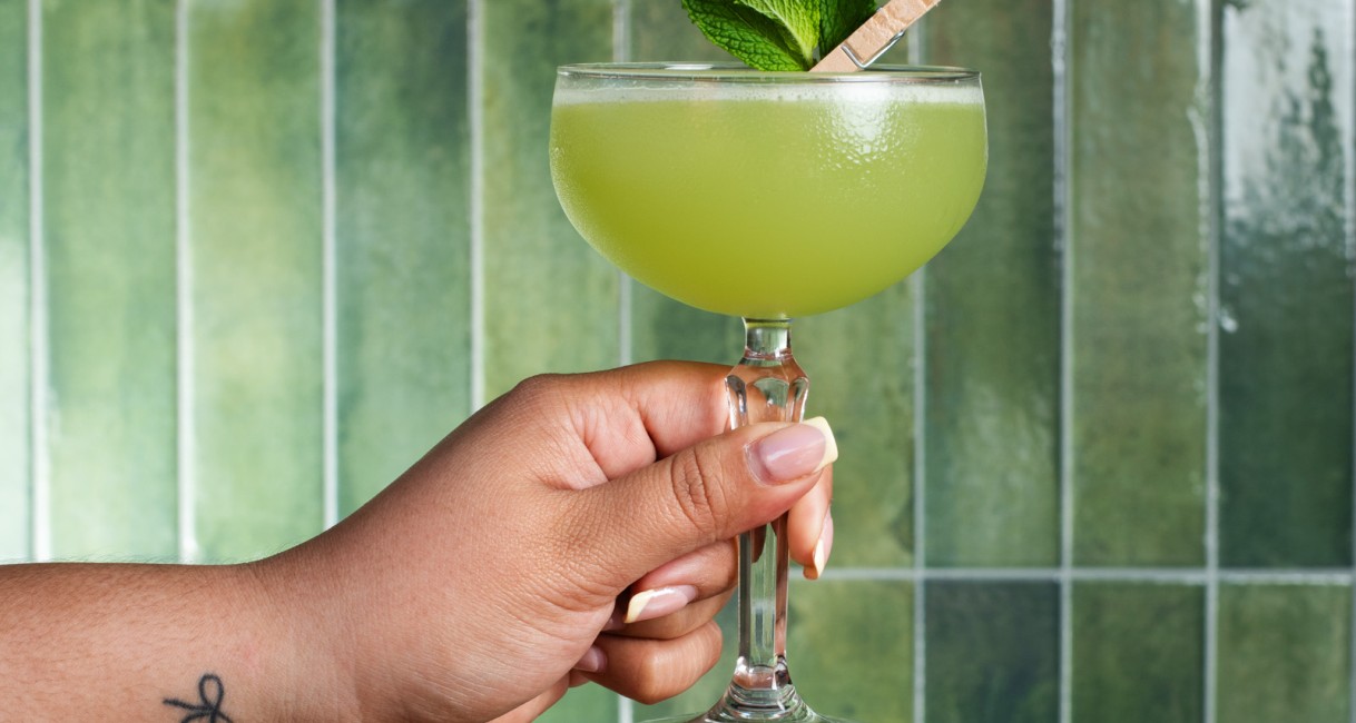 a hand holding a glass of green liquid