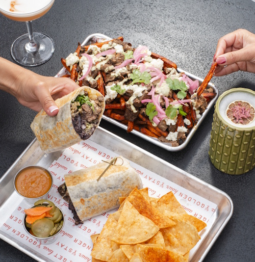 a person holding a burrito and a plate of food