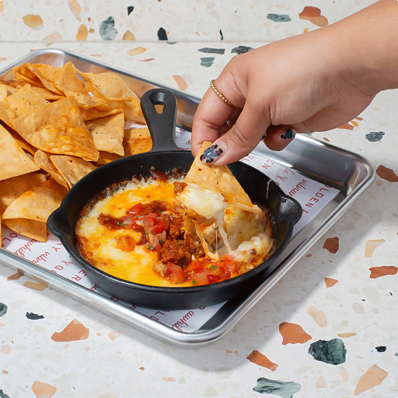 a hand dipping a chip into a skillet of food