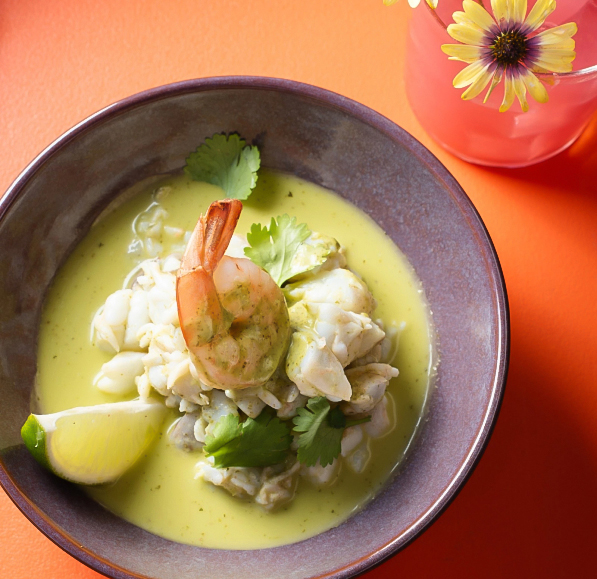 a bowl of soup with shrimp and lime wedges