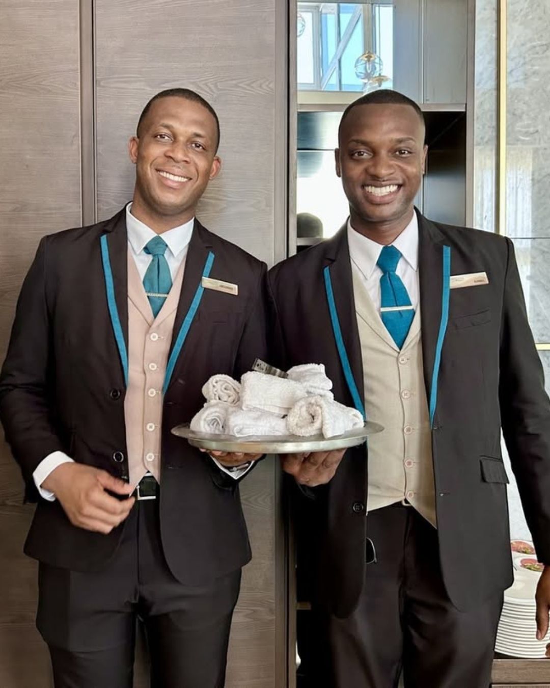 two men in suits holding a tray of towels
