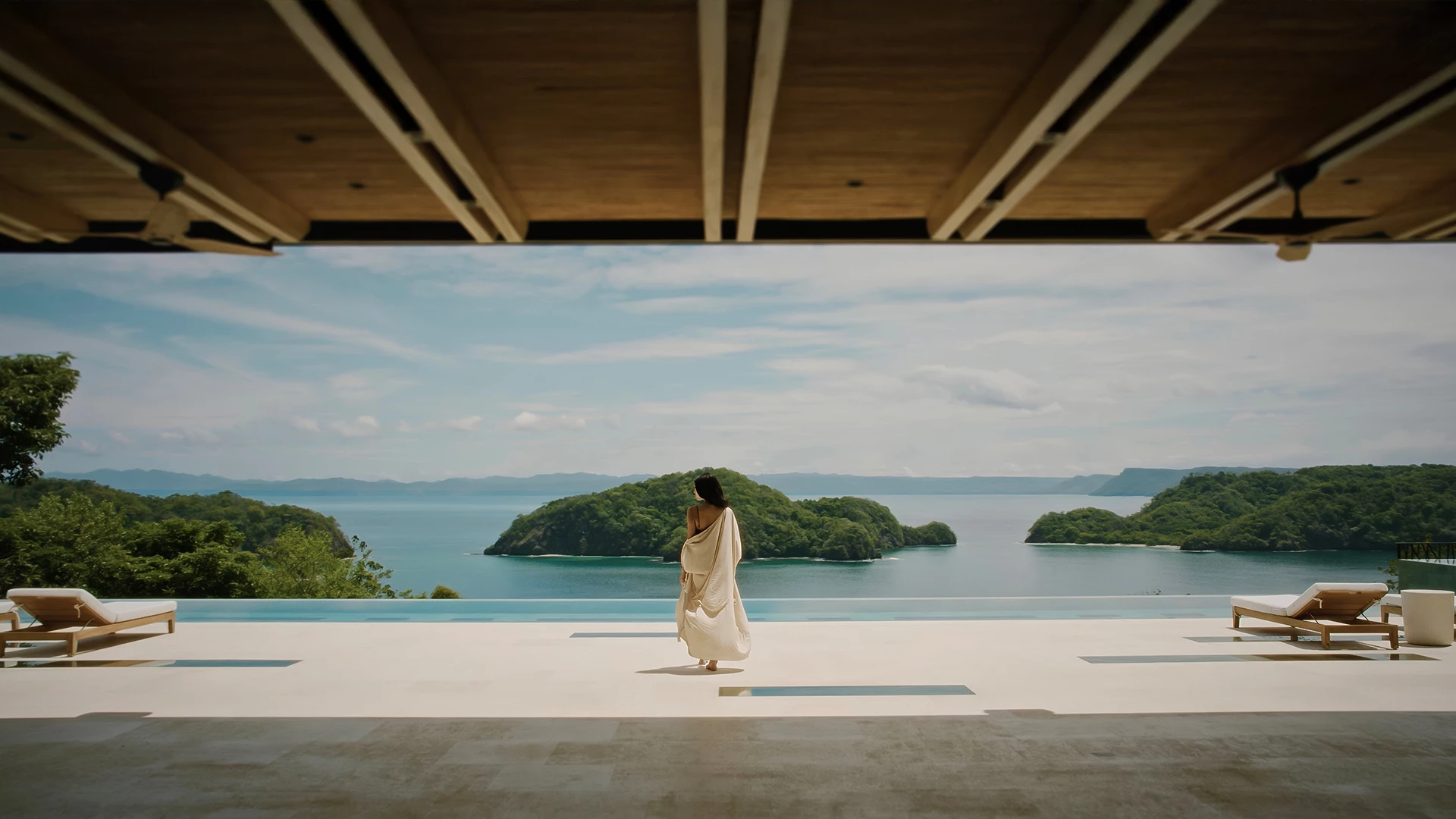 a woman in a white robe walking on a deck overlooking water