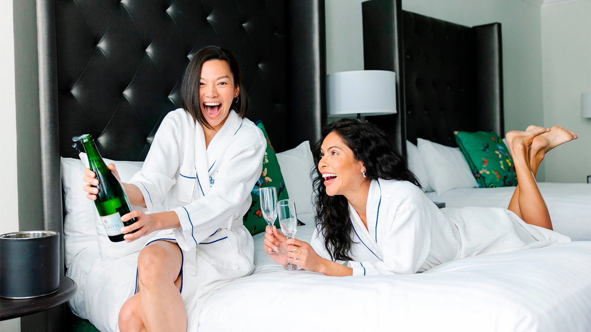two women in white robes holding wine glasses and smiling
