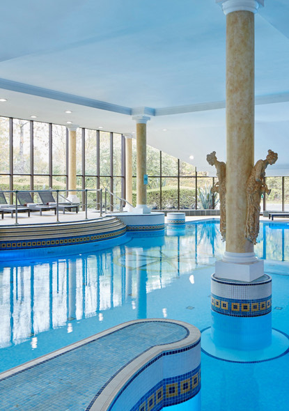An indoor pool with lots of tall windows and natural light coming in.