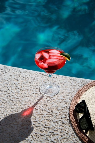 a glass of red liquid with ice and lime on a ledge