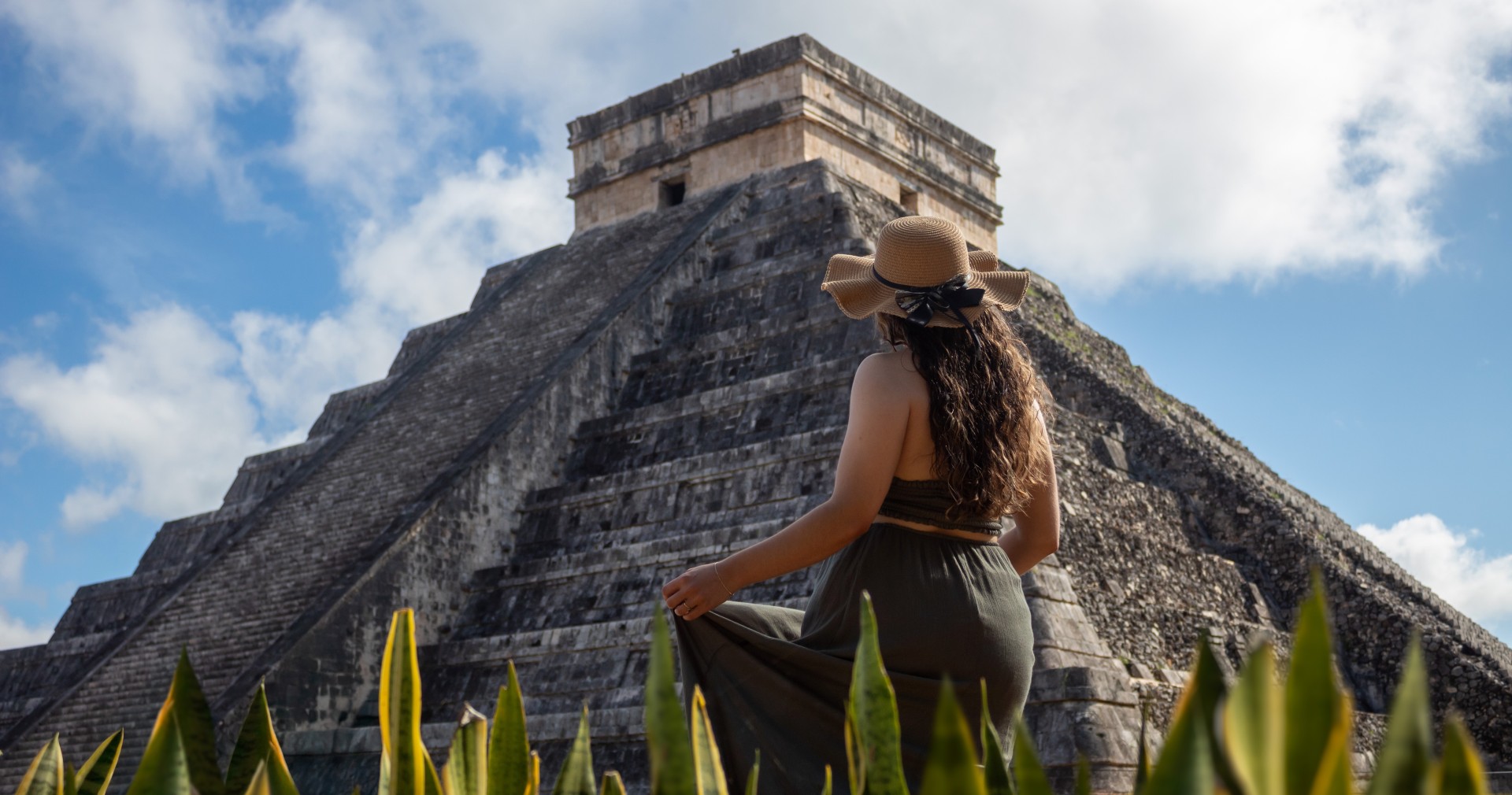 a woman in a dress and hat in front of a pyramid