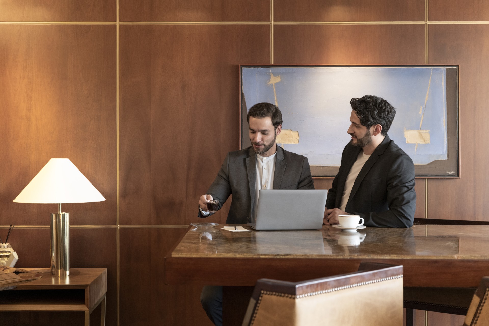two men sitting at a table looking at a laptop