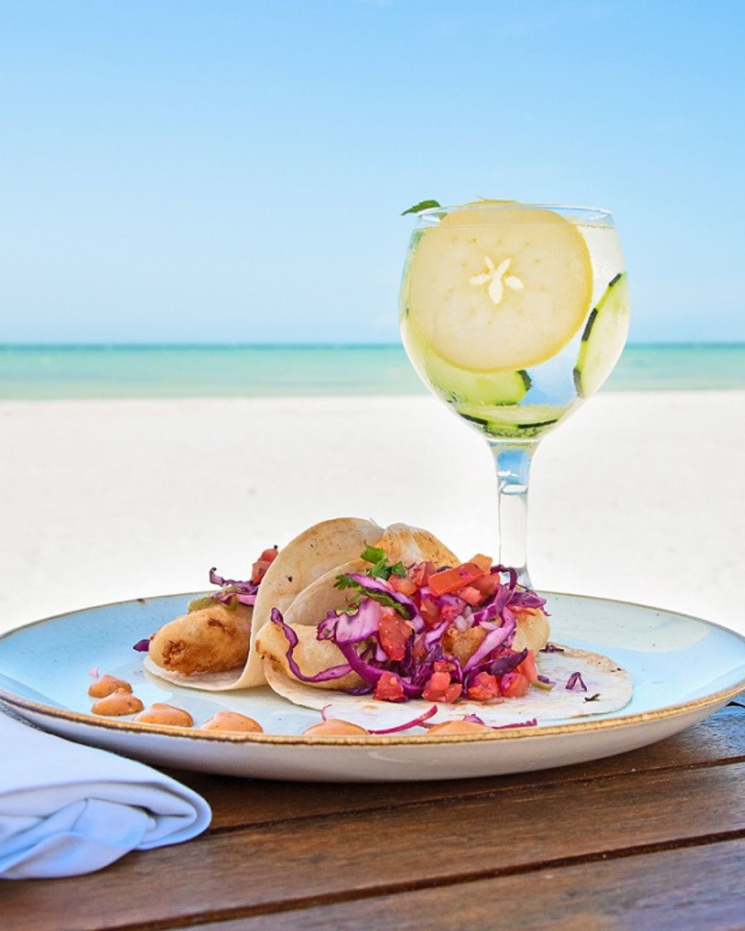a plate of tacos and a glass of water on a beach