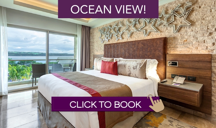 a bed with a large headboard and a window with a view of the ocean