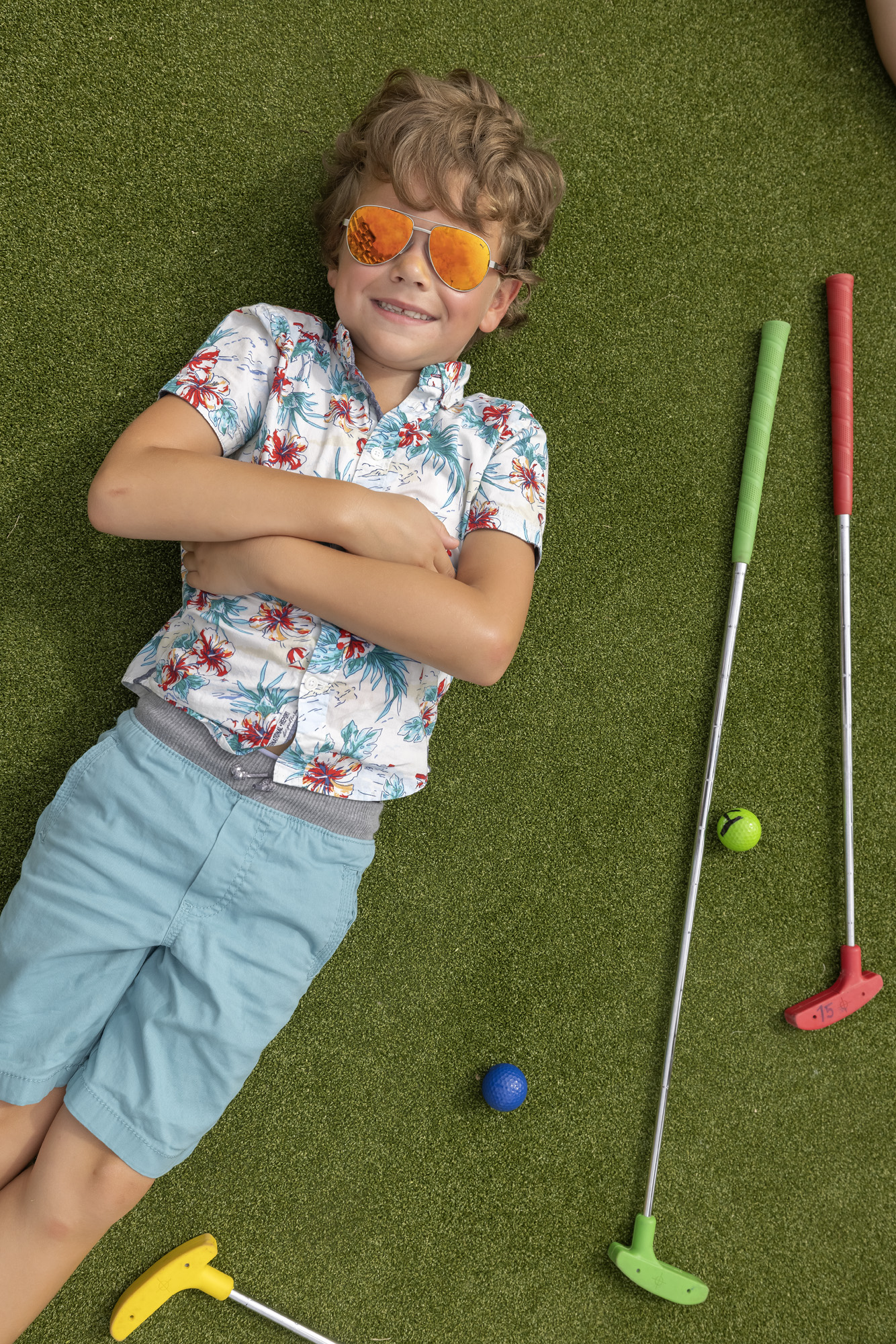 a boy lying on the ground with golf clubs and balls