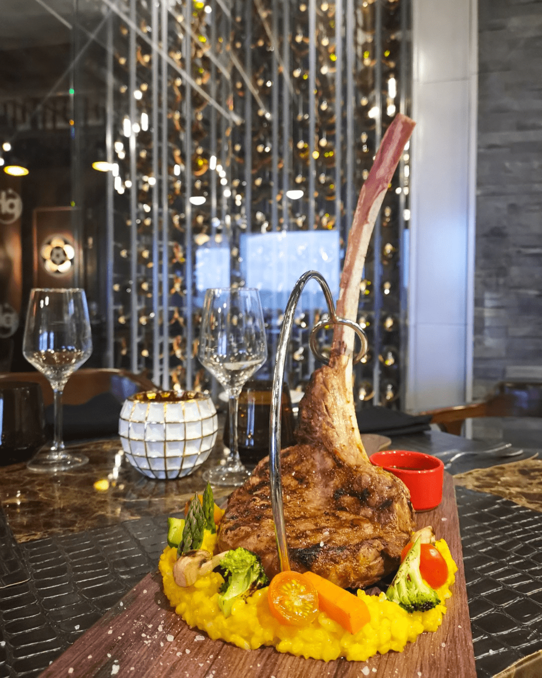 a steak on a platter with vegetables and wine glasses