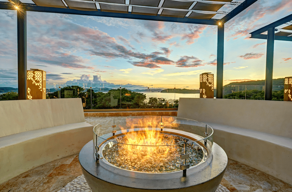 a fire pit with a glass top and a bench in front of a sunset