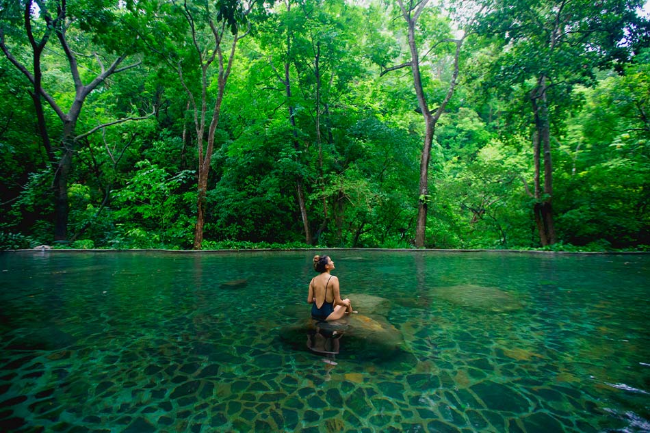 a woman sitting in a pool of water surrounded by trees