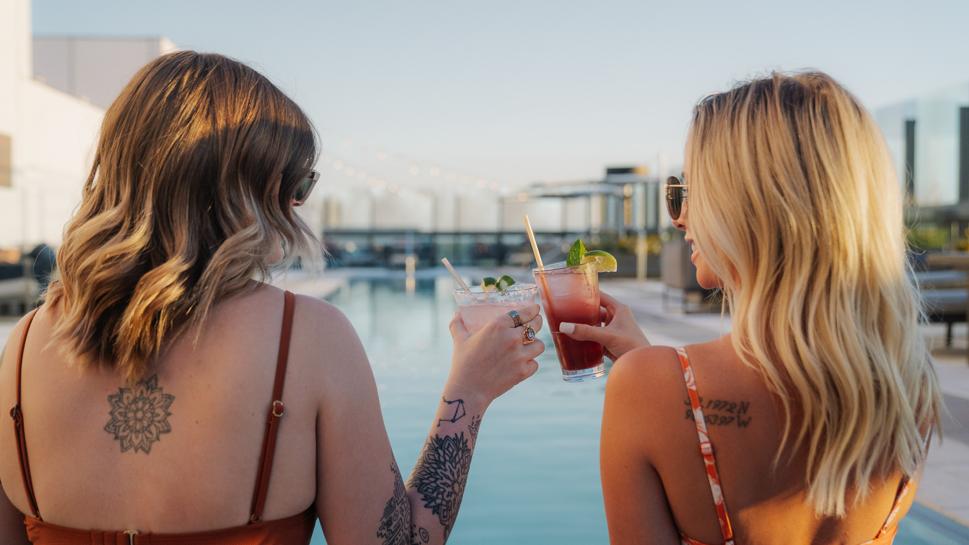 two women holding drinks by a pool
