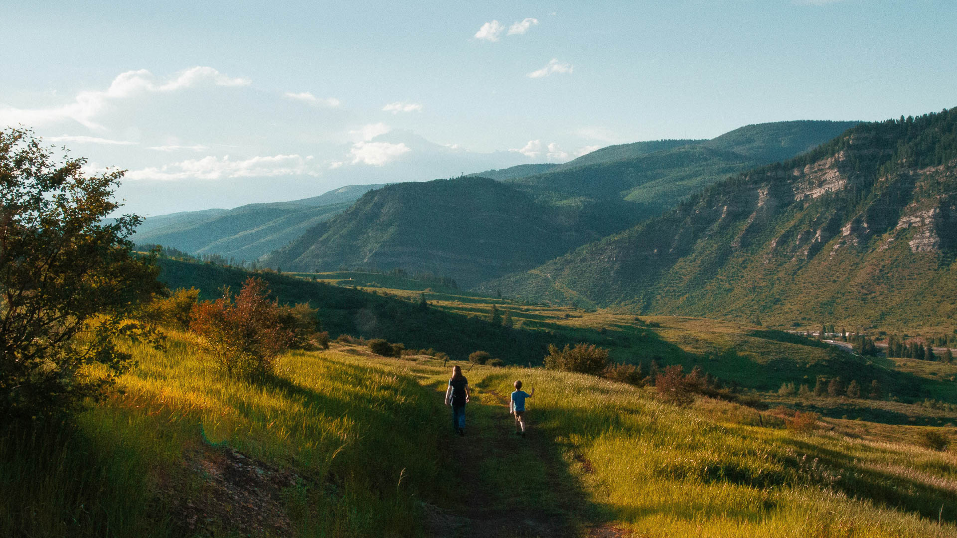 two people walking on a path in a grassy valley