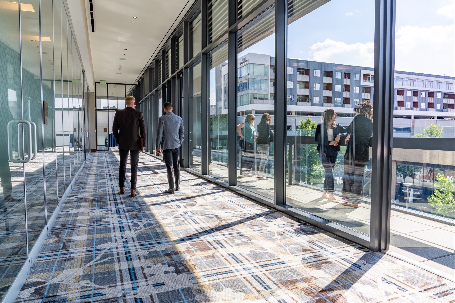 people walking through a hallway with large windows
