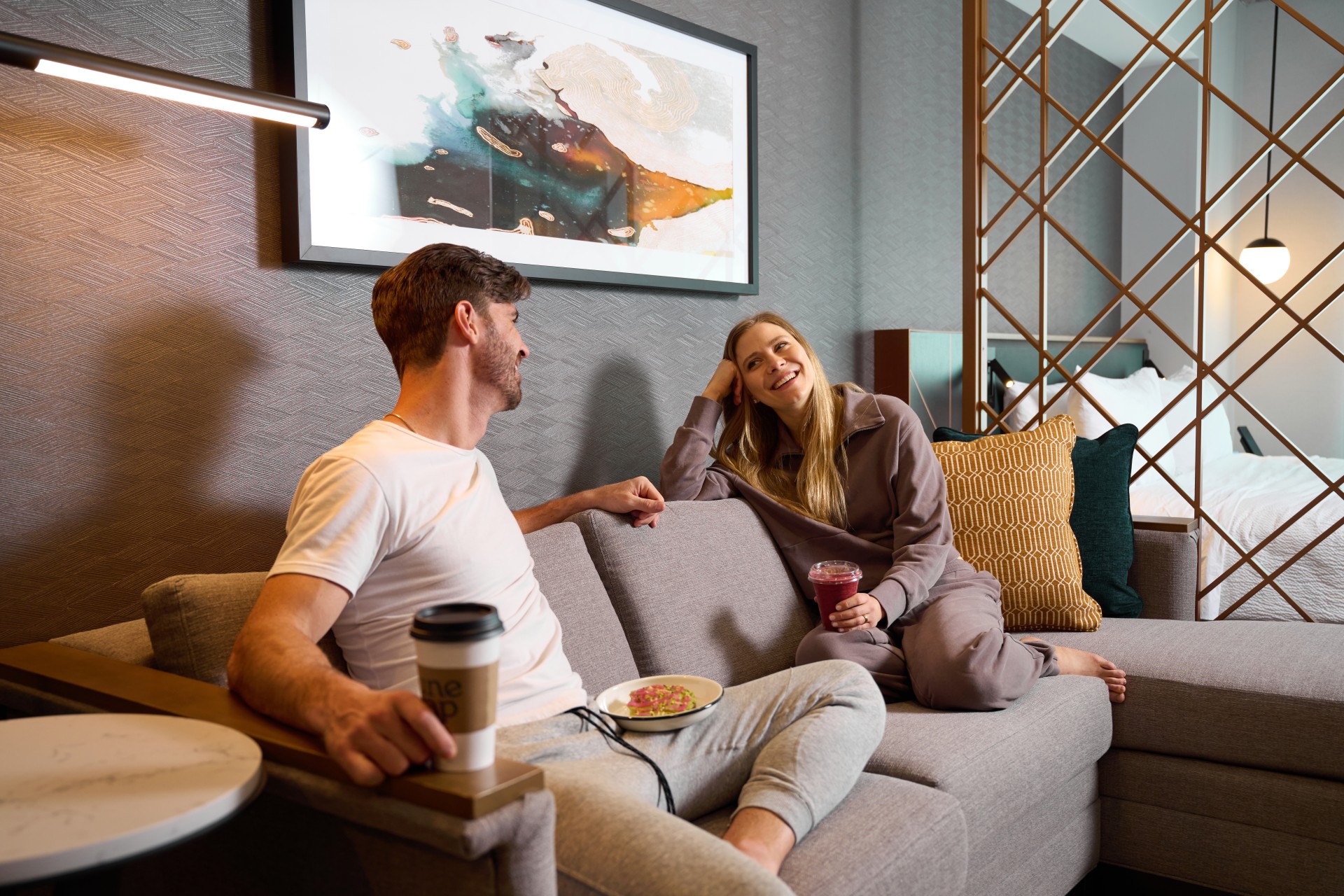 a man and woman sitting on a couch in an Apiary Hotel guest room